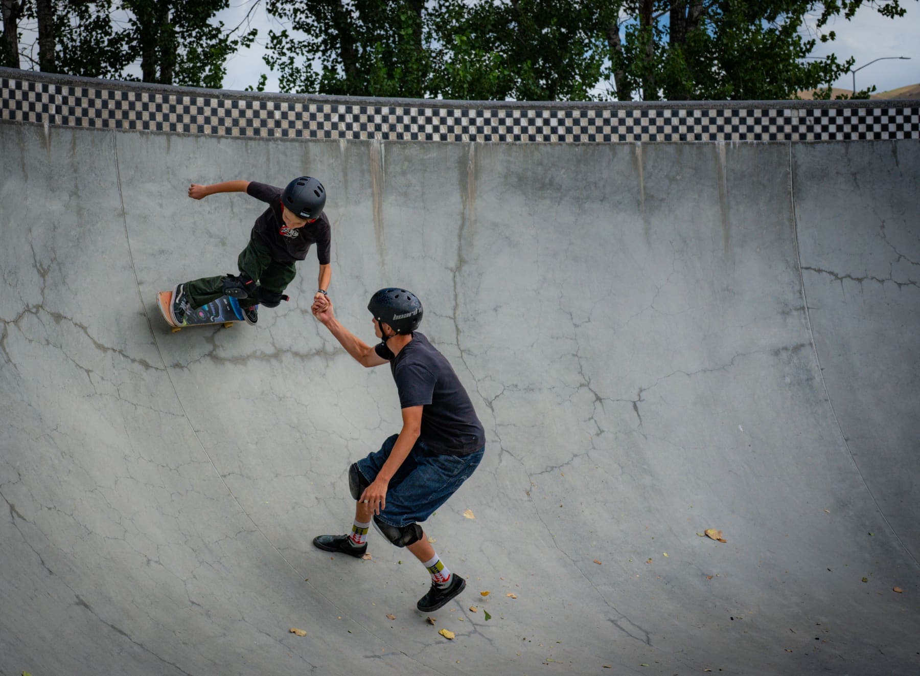 Coach holding a young skater's hand, guiding them down the bowl wall